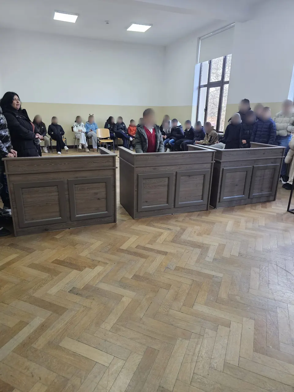 Într-o sală de judecată: un elev stă în boxă, iar colegii lui urmăresc de pe scaune